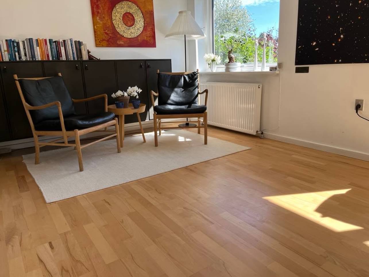 Klinikkens samtalerum med to lænestole i eg og sort læder, et lille bord med hvide orkidéer og et stort vindue ud mod haven.